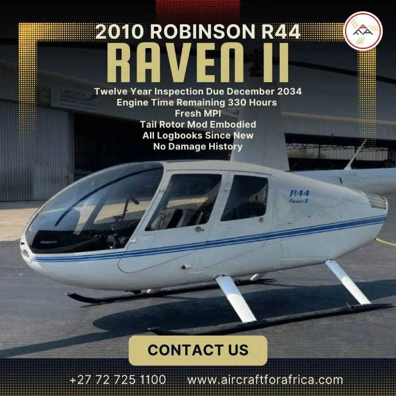A white Robinson R44 Raven II helicopter with blue stripes, viewed from the front-right, parked on an asphalt surface with a hangar in the background.