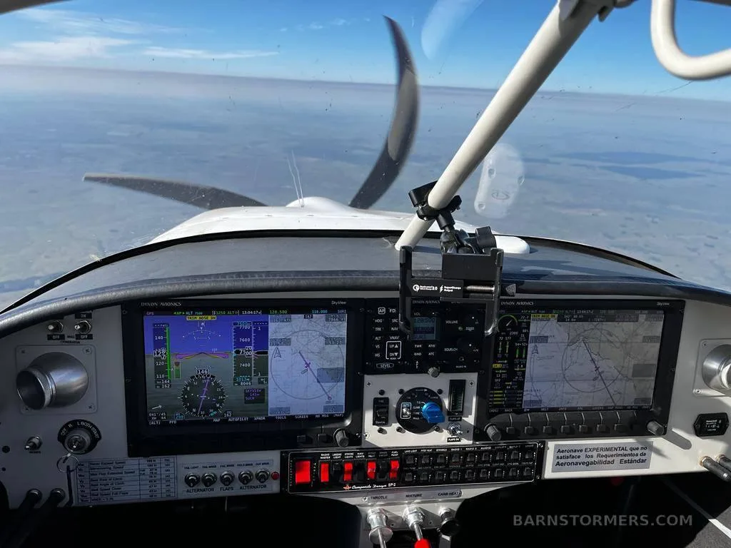 The cockpit of an aircraft in flight, showing the instrument panel with multiple digital displays and the propeller visible through the windshield.