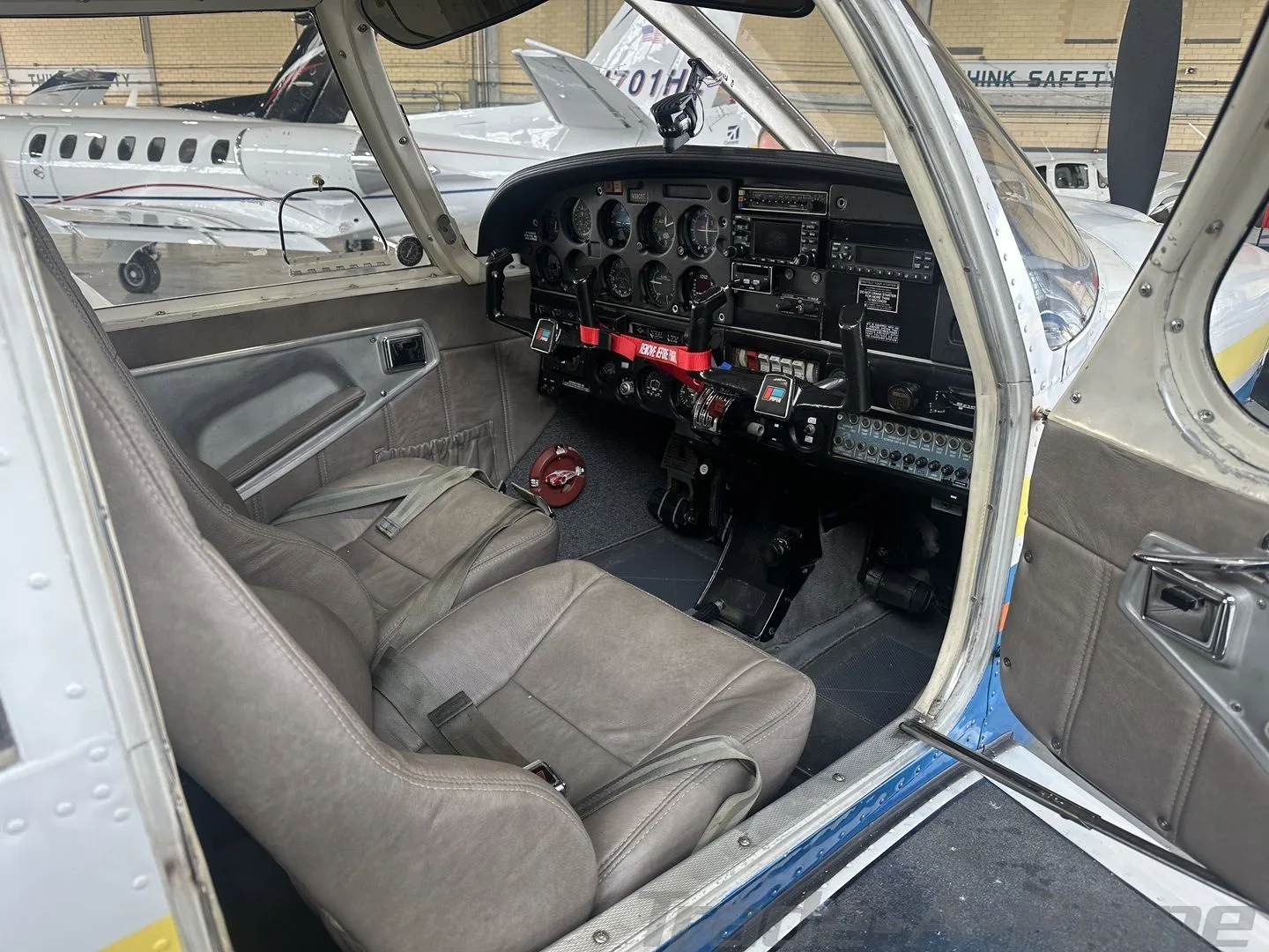 The cockpit of a light aircraft, N3905T, showing the instrument panel, controls, and two front seats inside a hangar.
