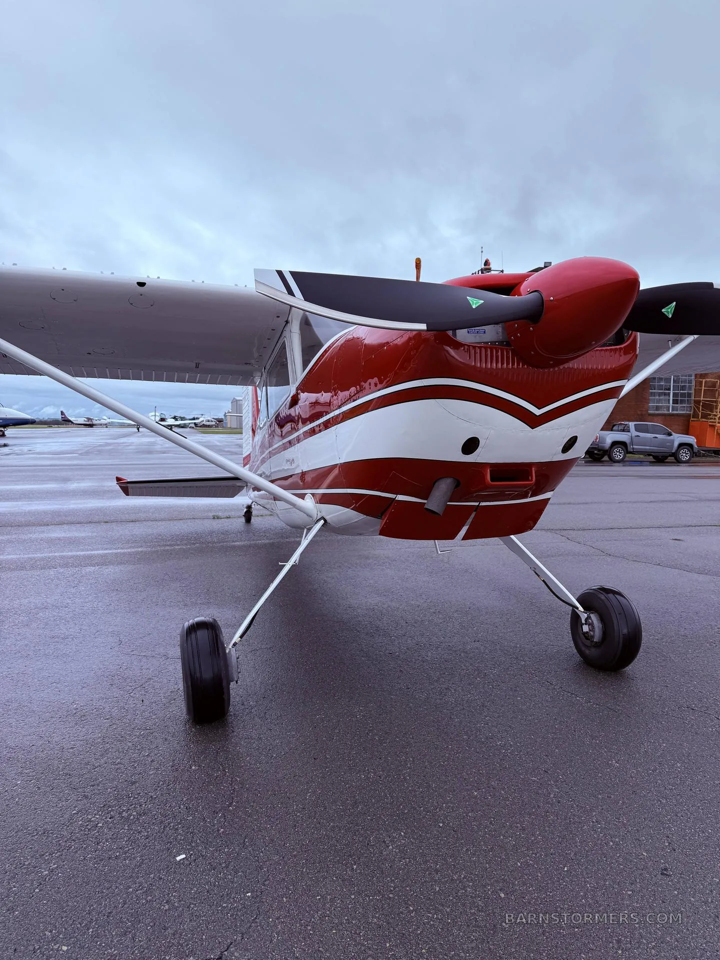A red and white single-engine propeller aircraft is parked on a wet tarmac, viewed from the front.