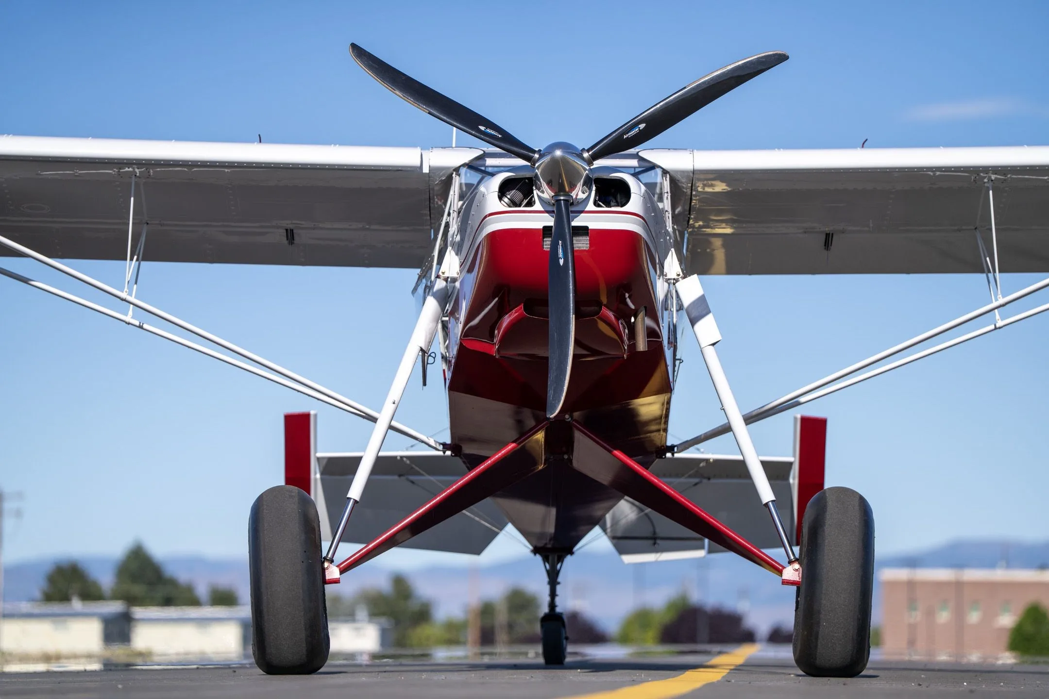 Head-on view of a red and white Just Aircraft SuperSTOL with large tundra tires on an airfield.