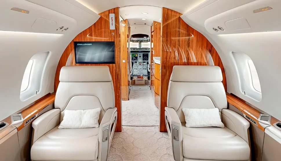 View from the private jet cabin looking forward, showing beige seats and the cockpit through the open door.