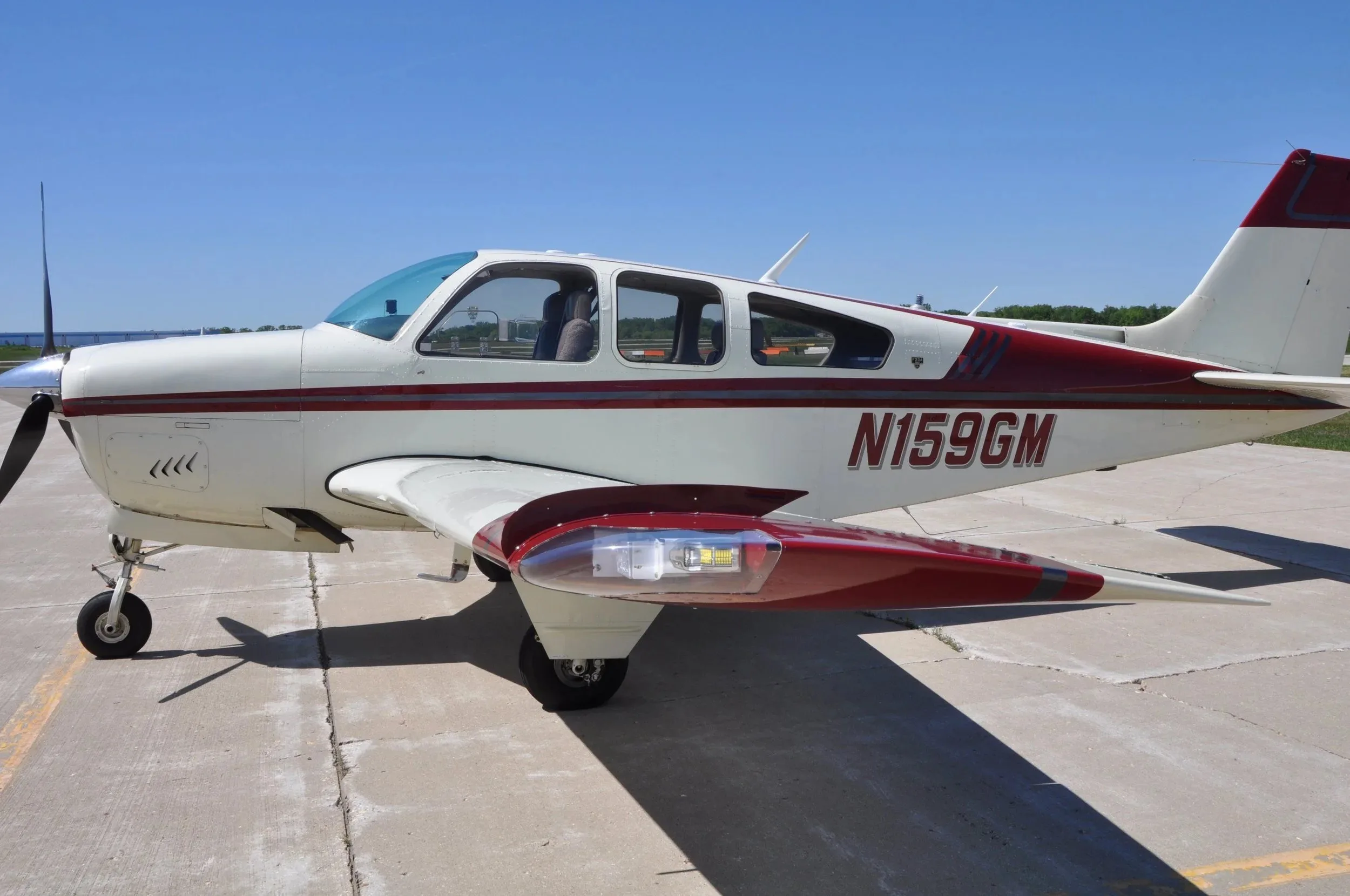A side view of the white and maroon Beechcraft Bonanza F33A N159GM showing the registration and wingtip.