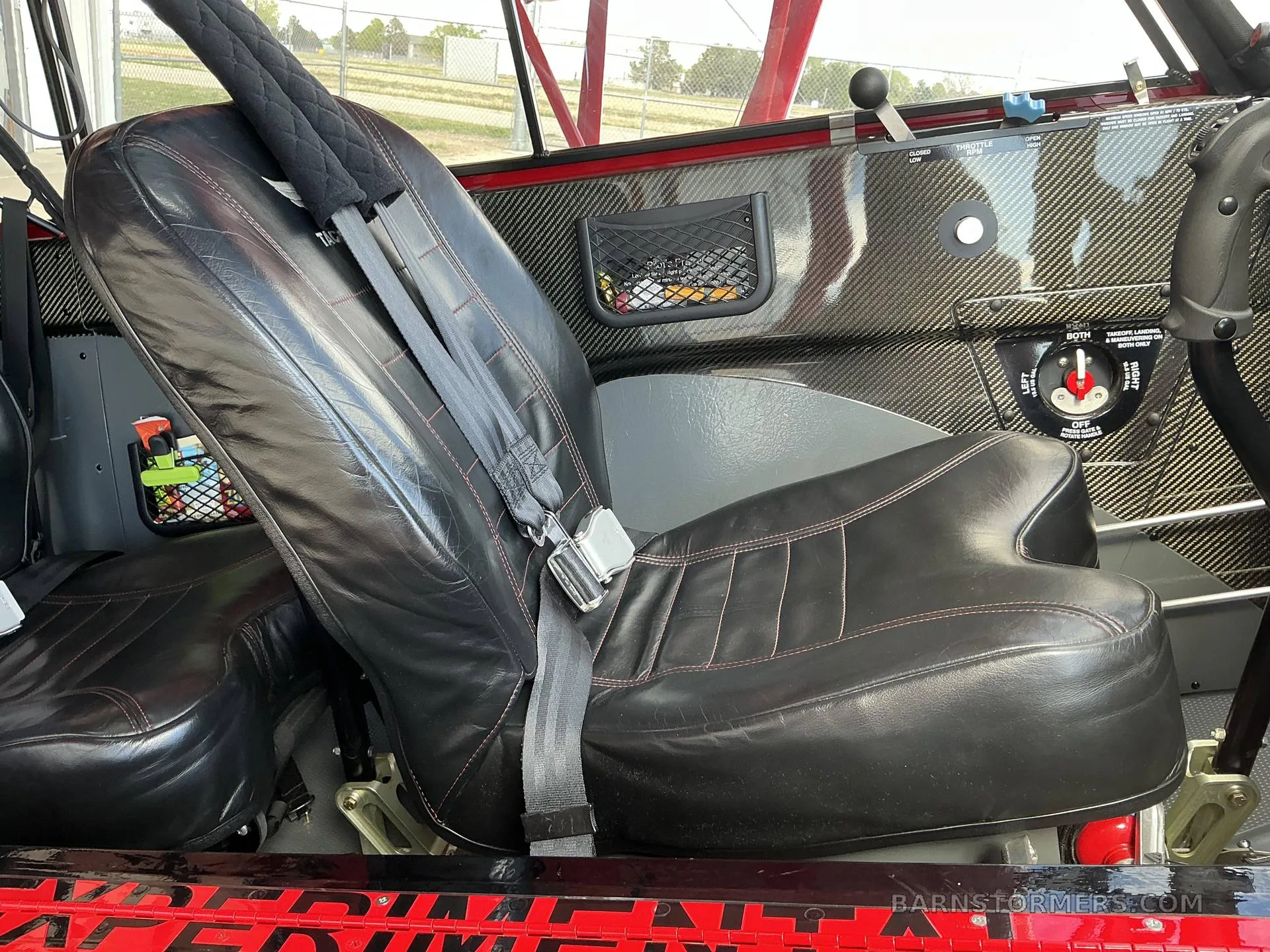 The black leather seats with red stitching inside a red aircraft cabin, showing a carbon fiber panel.