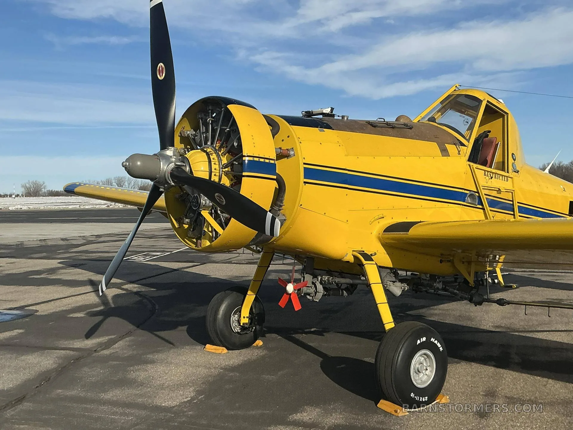 A yellow agricultural aircraft with blue stripes, registration N432DA, parked on an airfield under a blue sky.
