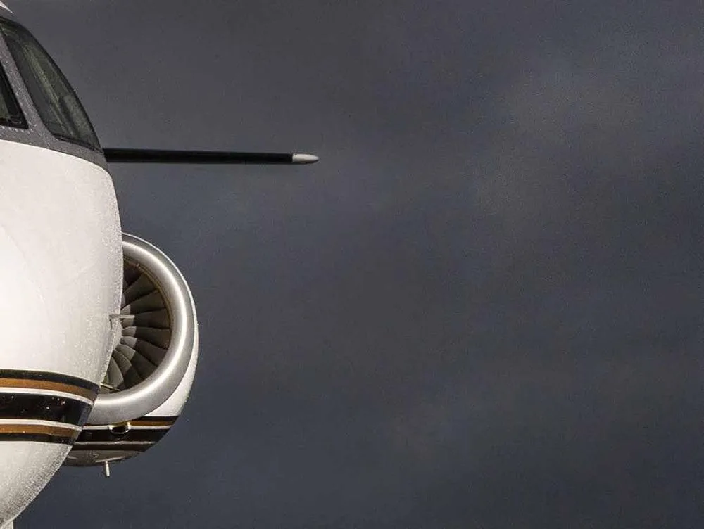 A close-up of the front fuselage and engine of a white business jet with gold and black stripes against a dark sky.
