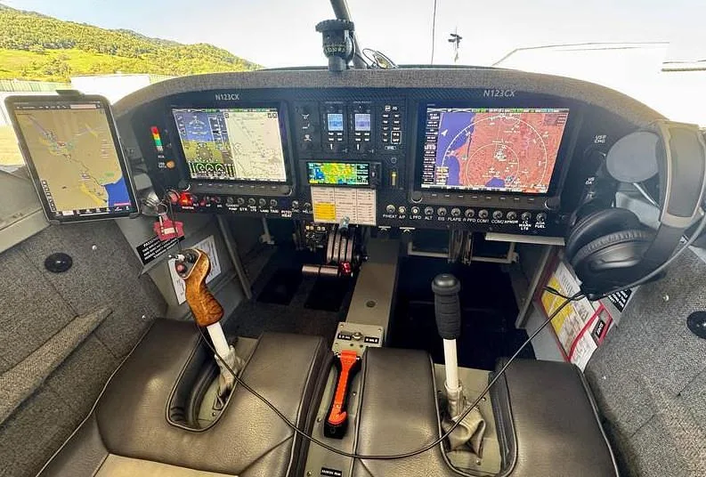 The cockpit of the N123CX aircraft, showing the instrument panel with multiple screens, controls, and two seats.