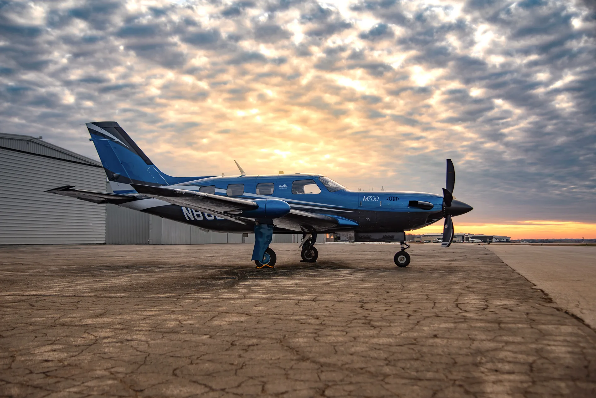 A blue and black M700 aircraft sits on the tarmac at sunset.
