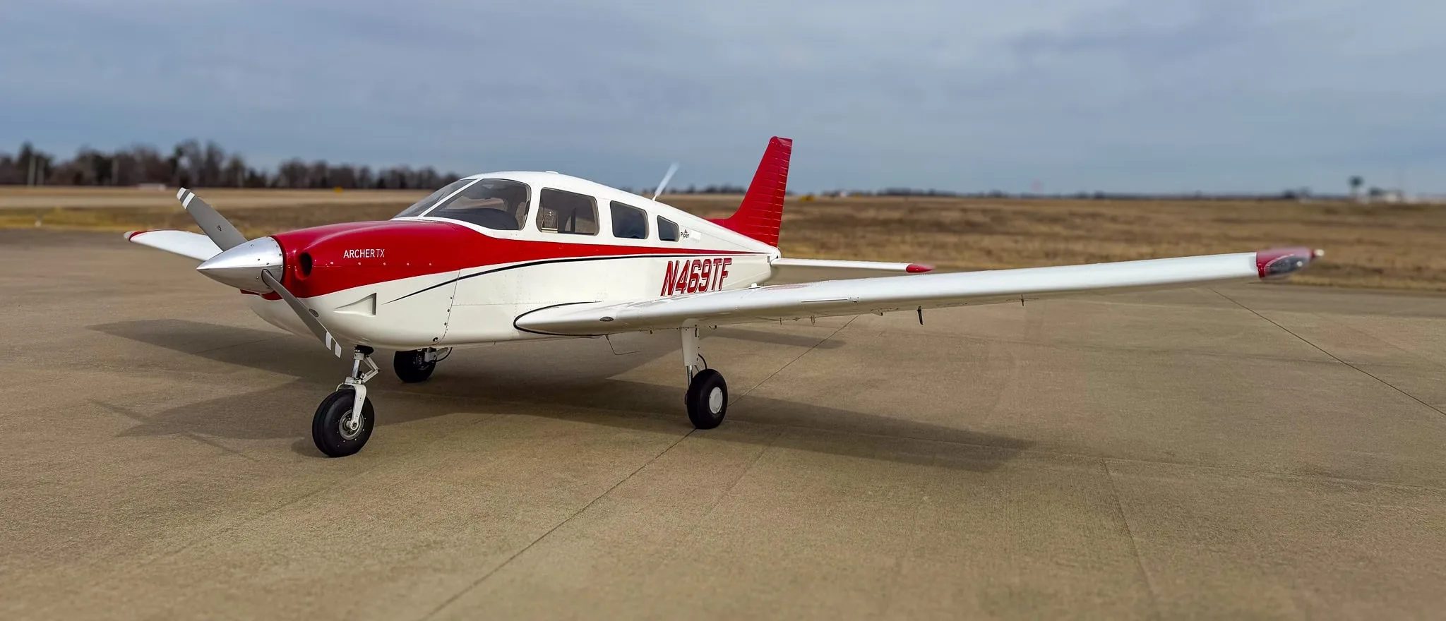 A white and red Piper Archer TX aircraft, N469TF, parked on an airfield under a cloudy sky.