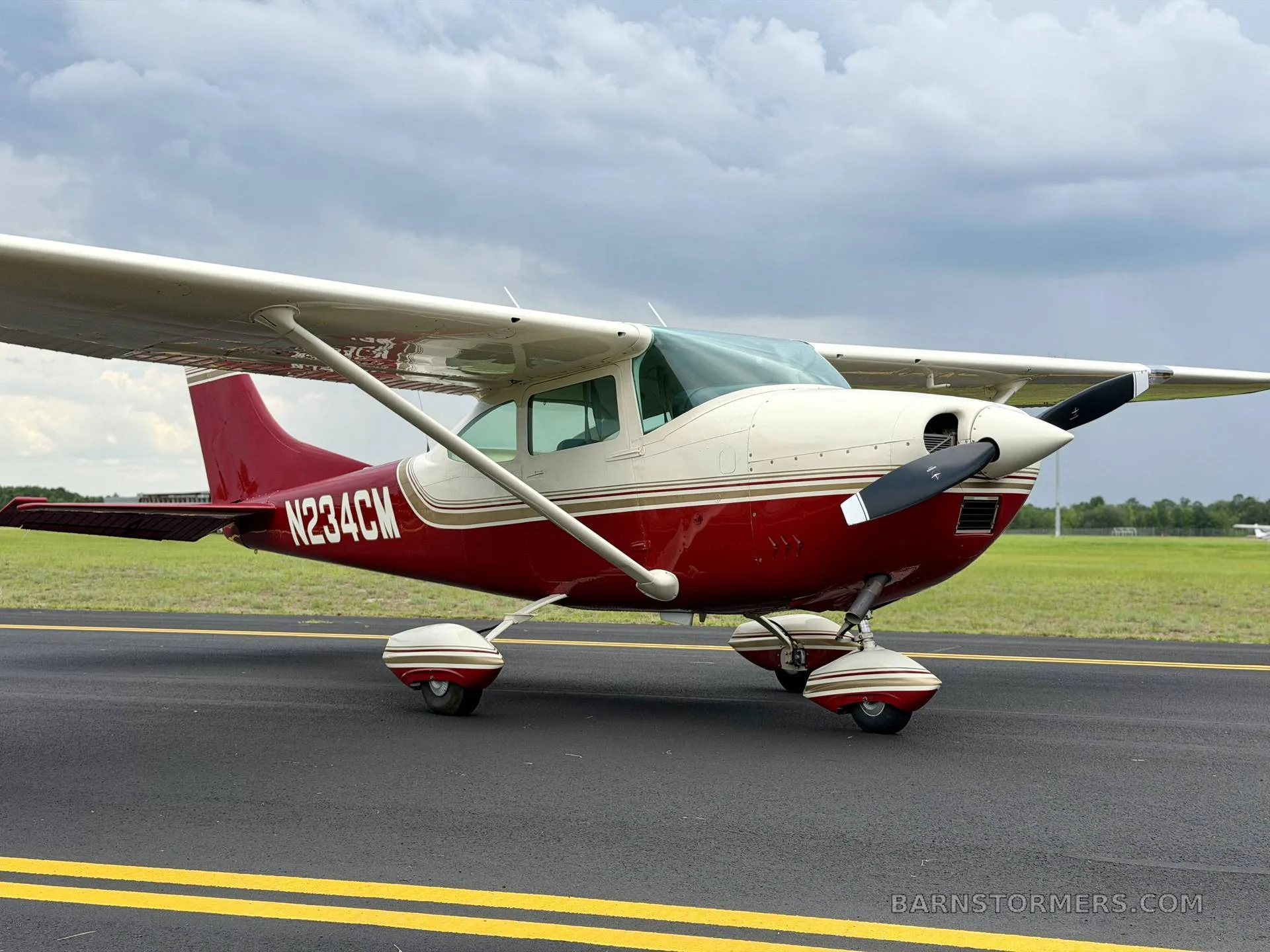 A front-right view of a red and white single-engine high-wing aircraft with registration N234CM on an airfield tarmac.