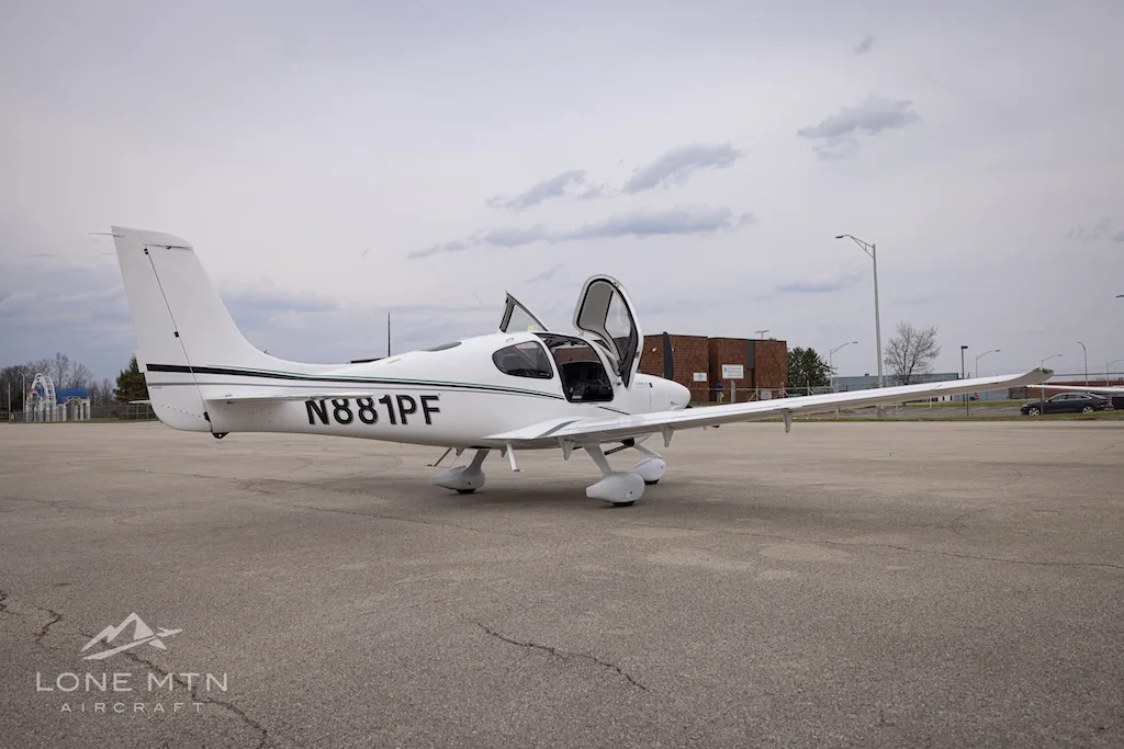 A white Cirrus SR22 aircraft with N881PF registration and open doors, parked on an asphalt ramp with buildings in the background.