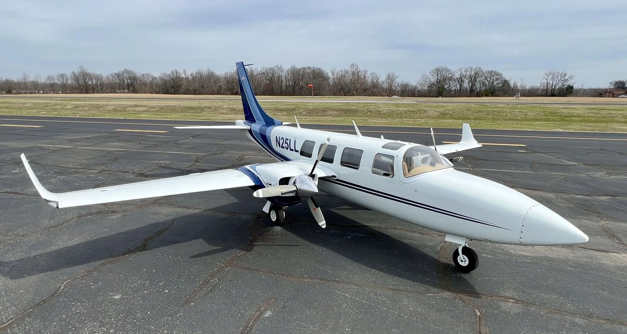 A white and blue twin-engine aircraft, N25LL, parked on an asphalt runway under a cloudy sky.