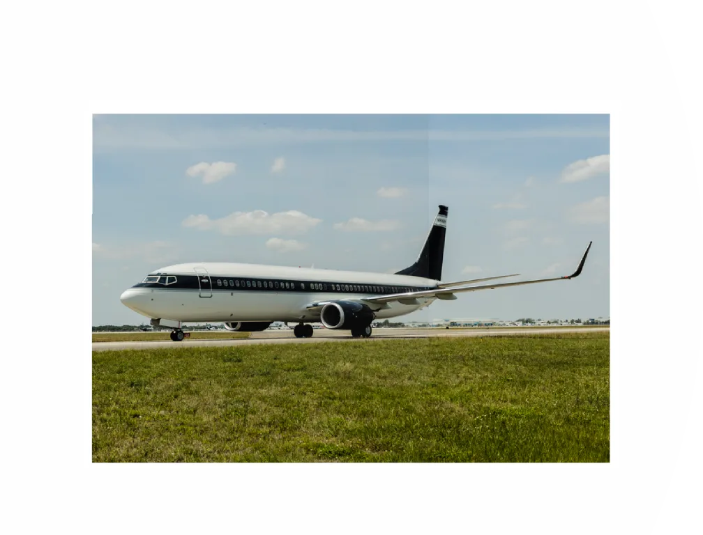 A Boeing 737 BBJ in a dark blue and white livery taxiing on a runway with green grass.