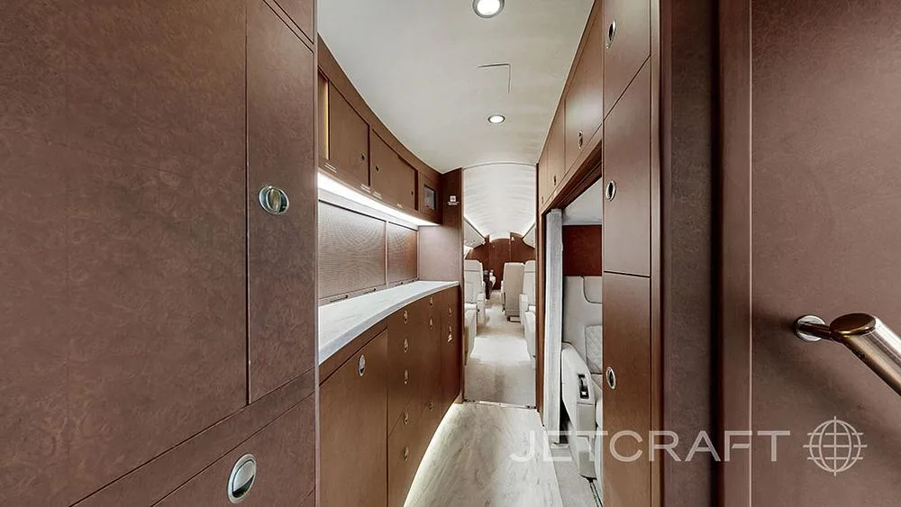 The aircraft's galley area features extensive wooden cabinetry and a light-colored floor, leading towards the rear.