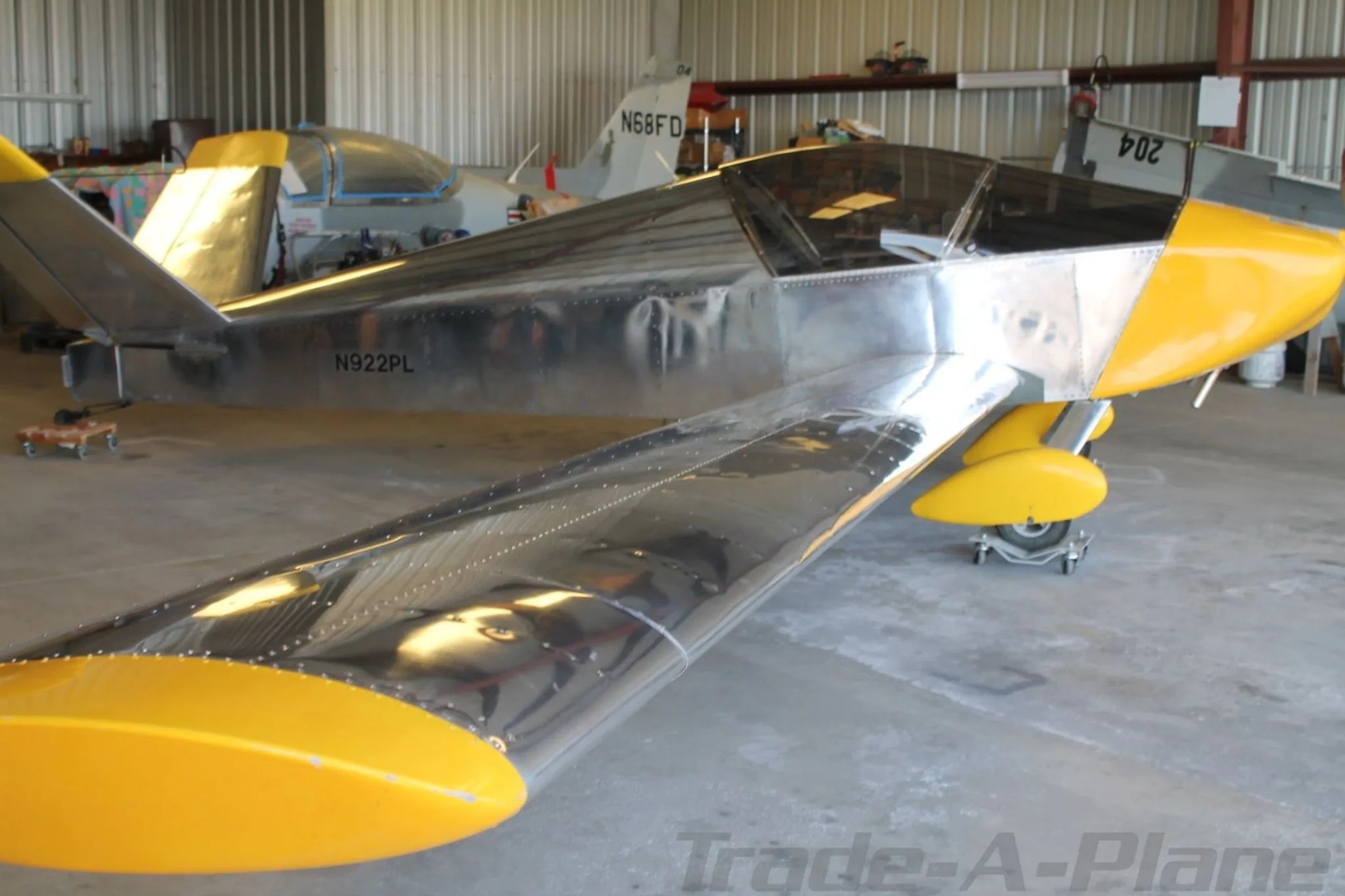 A partially assembled, unpainted metal aircraft with yellow accents and tail number N922PL, viewed from the rear-left in a hangar.