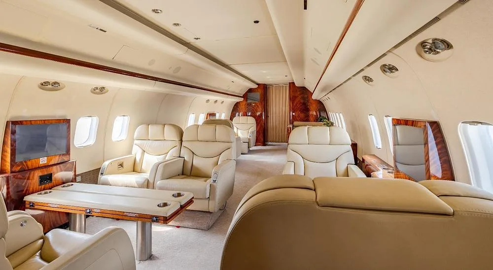 A luxurious aircraft interior with cream leather seats, wood tables, and polished wood paneling.