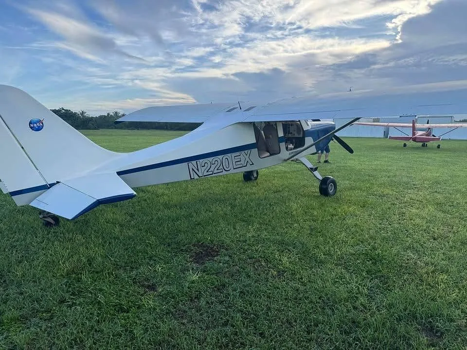 A rear view of the white and blue experimental aircraft N220EX with a NASA logo on its tail, parked on a grassy field.