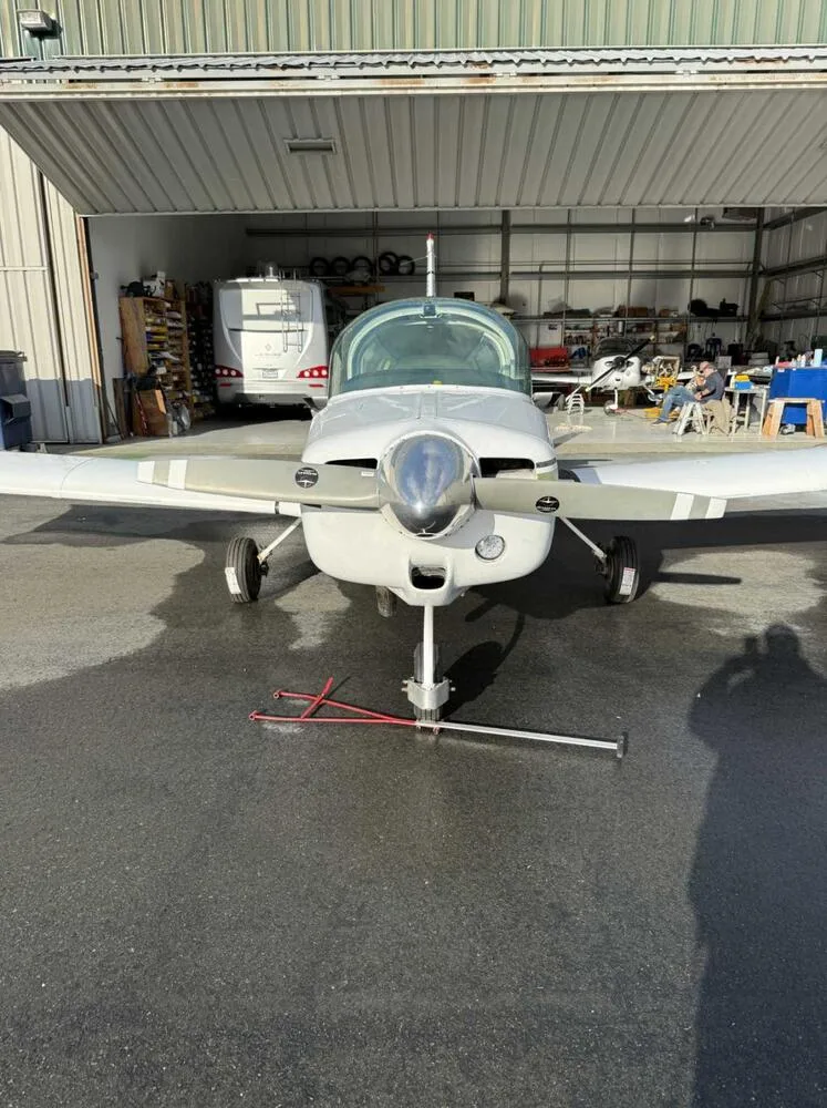 Front view of a white and green Grumman American AA-5 Traveler aircraft parked in front of a hangar.