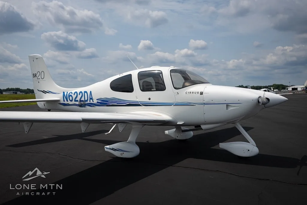 A side view of the white Cirrus SR20 aircraft N622DA with blue accents parked on an asphalt runway.