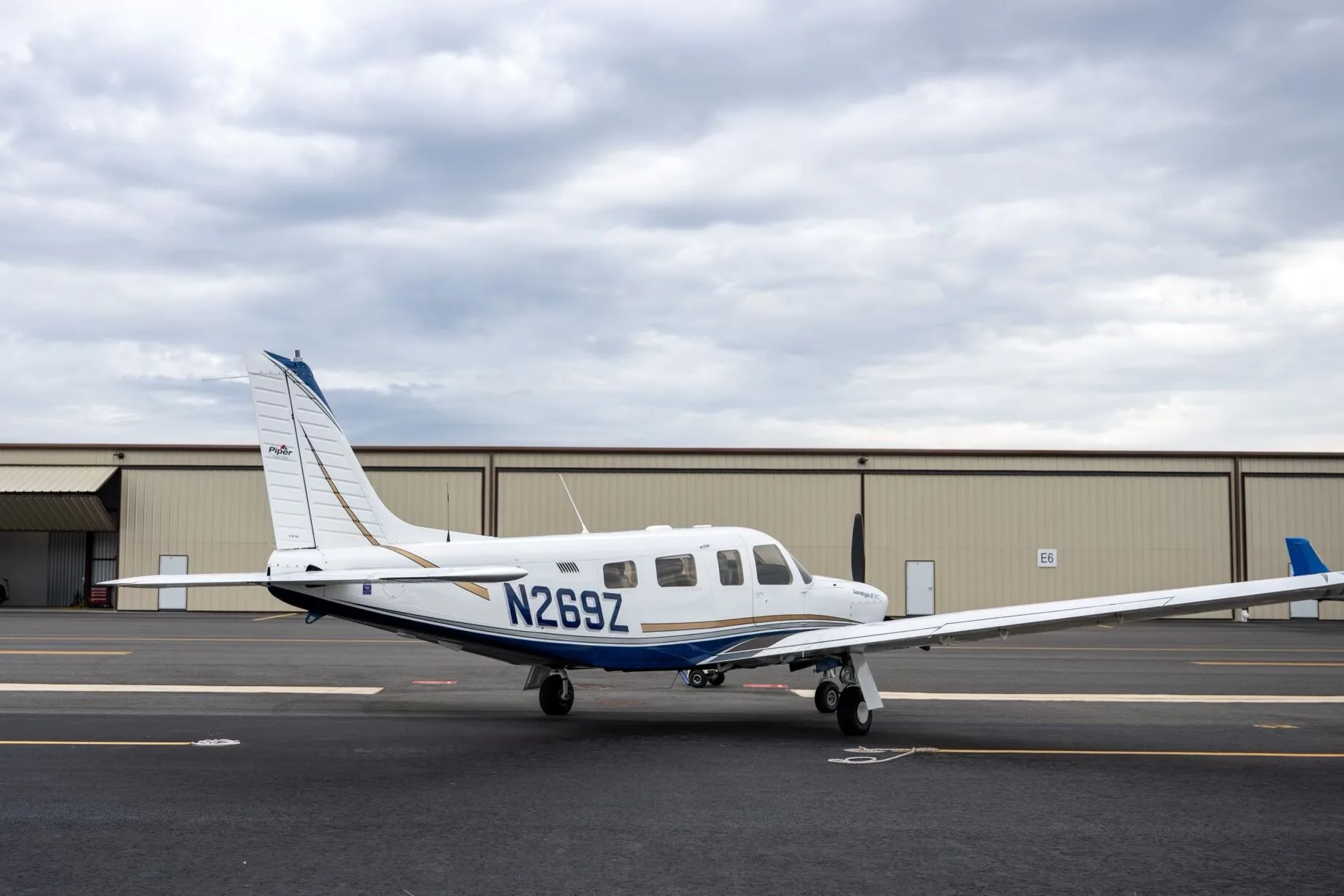 A side view of a white Piper Saratoga II TC aircraft, tail number N269Z, parked on the tarmac with hangars in the background.