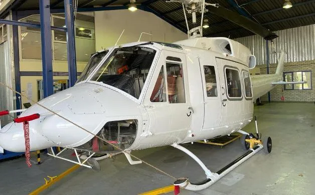 A white helicopter with "REMOVE BEFORE FLIGHT" tags on its nose, parked inside a hangar.