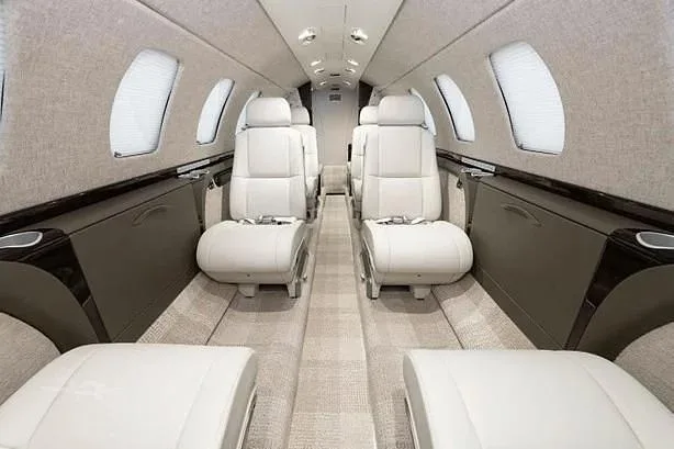 The aircraft's cabin features light-colored leather seats and a beige carpeted aisle.