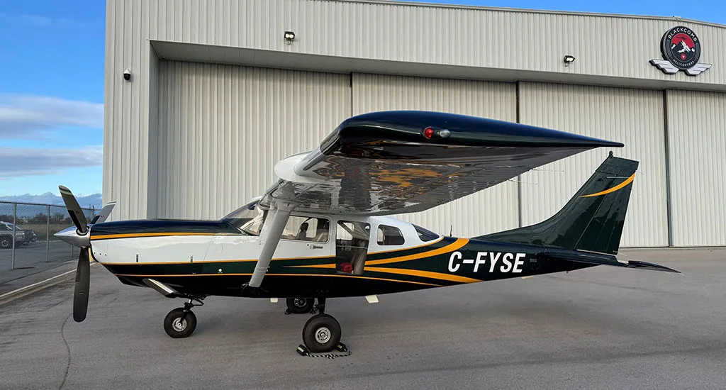 A side view of a dark green and white Cessna 182 with yellow stripes, registration C-FYSE, parked on an airfield.