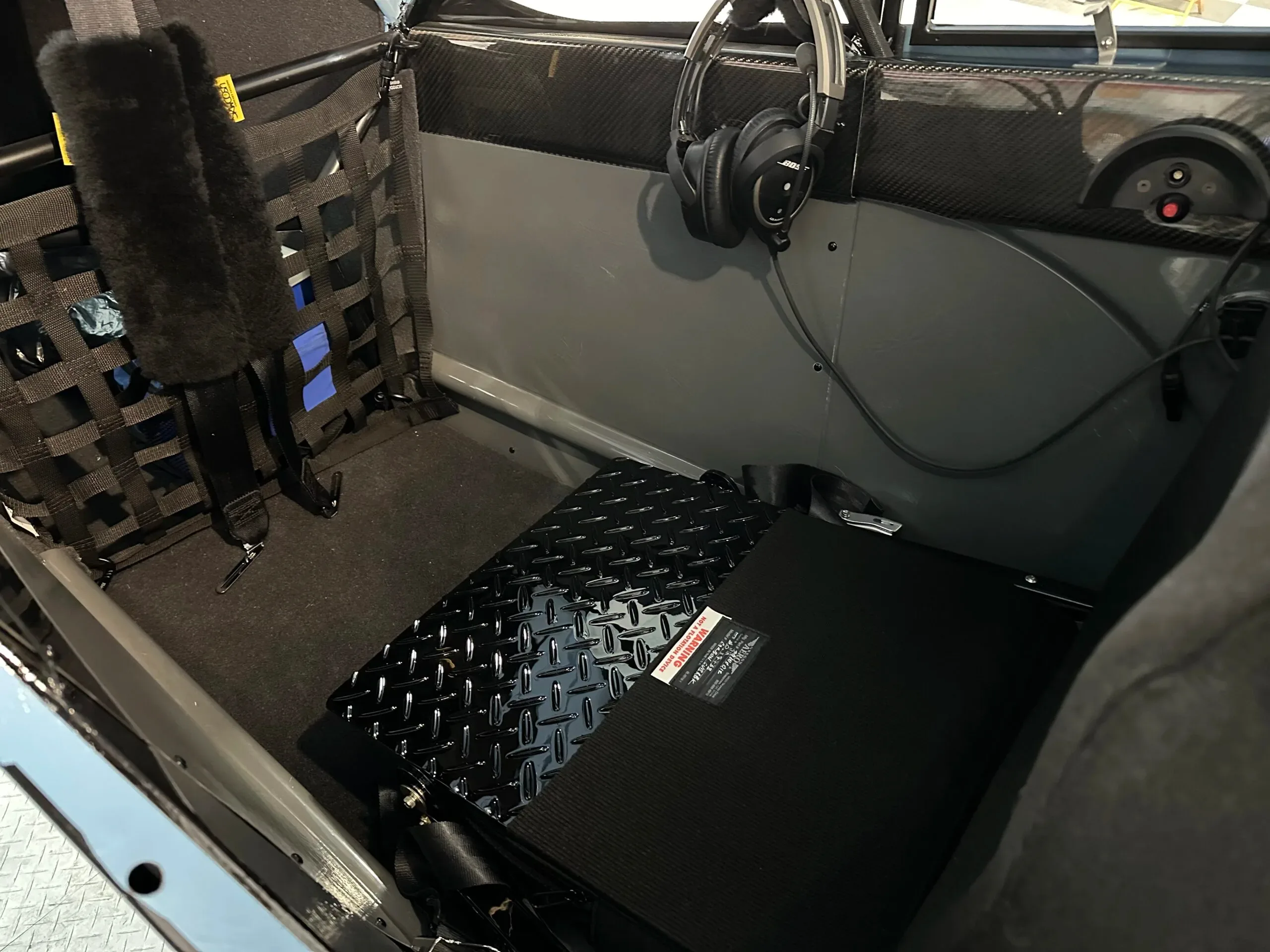 The rear cabin interior of the aircraft, showing a cargo net, headphones, and a diamond plate floor panel.