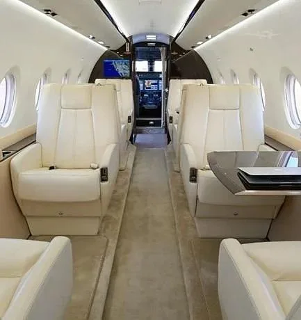 The luxurious interior of a private jet cabin with cream leather seats and a view towards the cockpit.