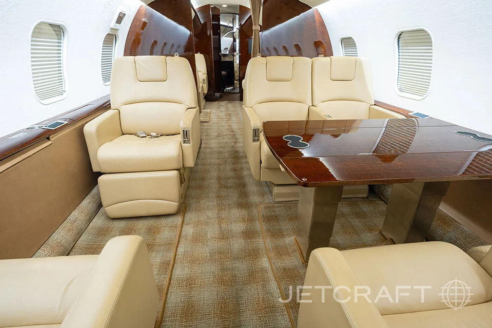 The private jet cabin interior with beige leather seats and a polished wooden dining table.