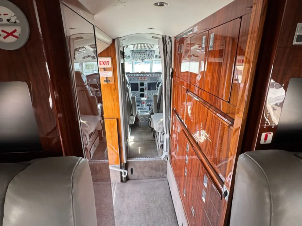View from the business jet cabin looking forward into the cockpit, flanked by polished wood cabinetry.
