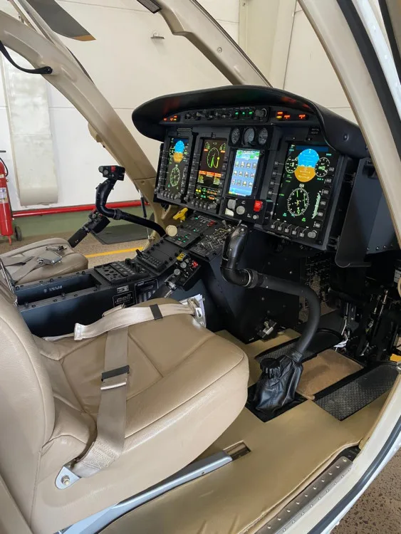 The cockpit of a Bell 429 helicopter featuring multiple digital screens, controls, and a tan pilot's seat.