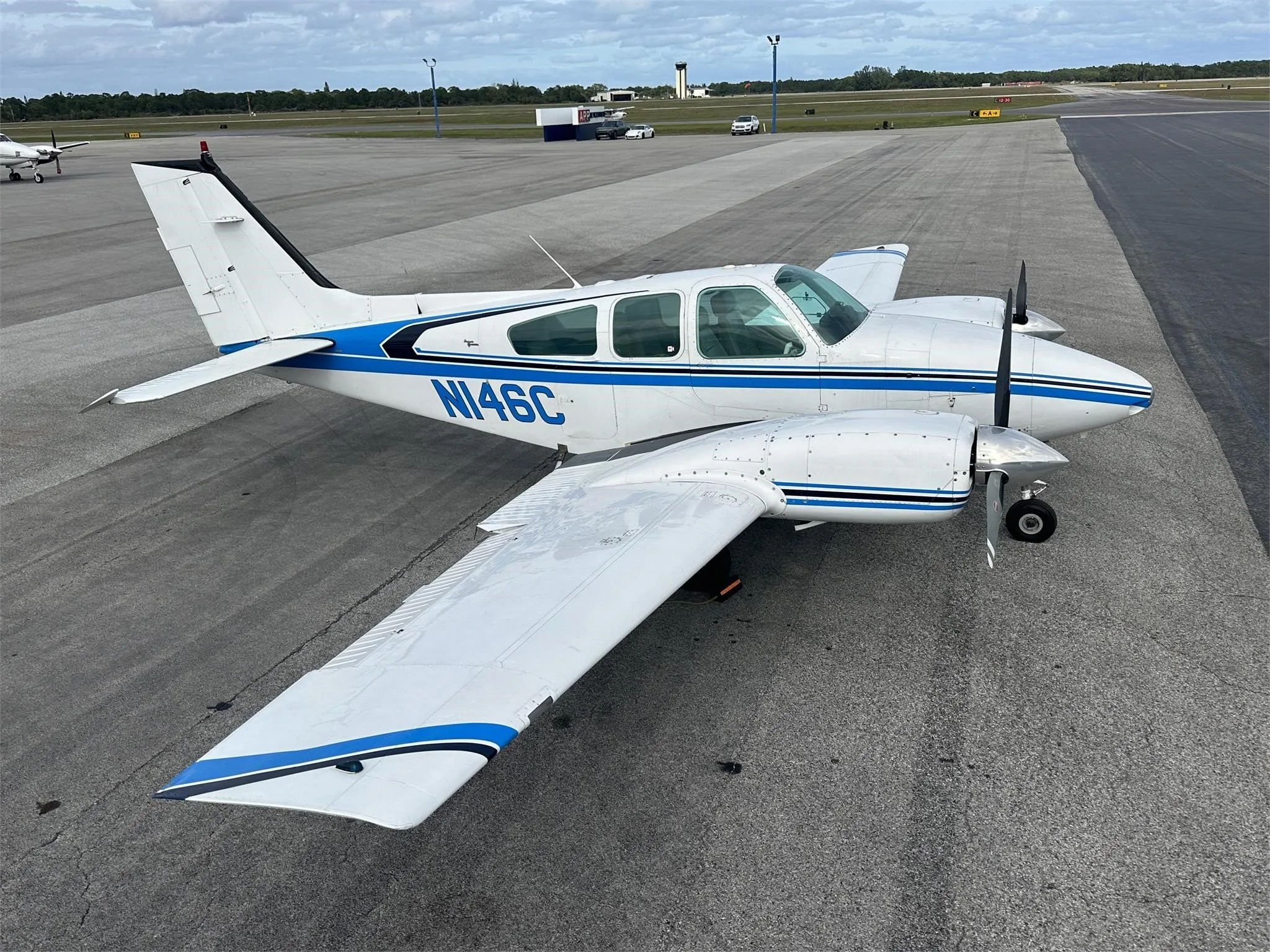 A white and blue twin-engine aircraft, N146C, parked on an airport tarmac with a distant control tower.