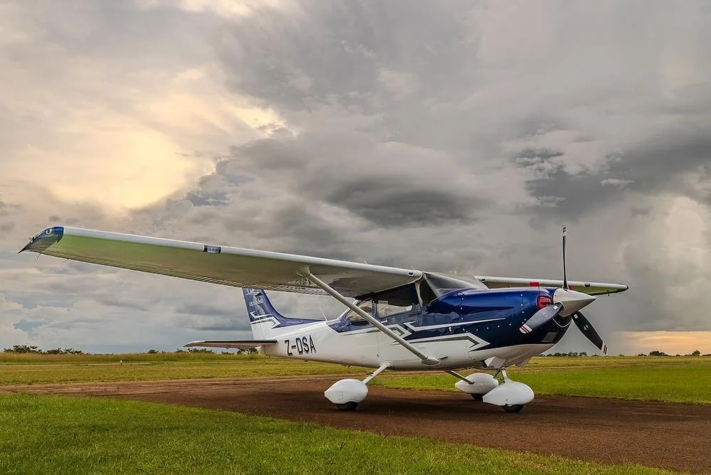 A side view of a blue and white Cessna Skylane (Z-DSA) on a tarmac under a cloudy sky.