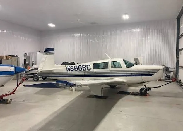 A white single-engine aircraft with blue and grey stripes, registration N888BC, parked inside a hangar.