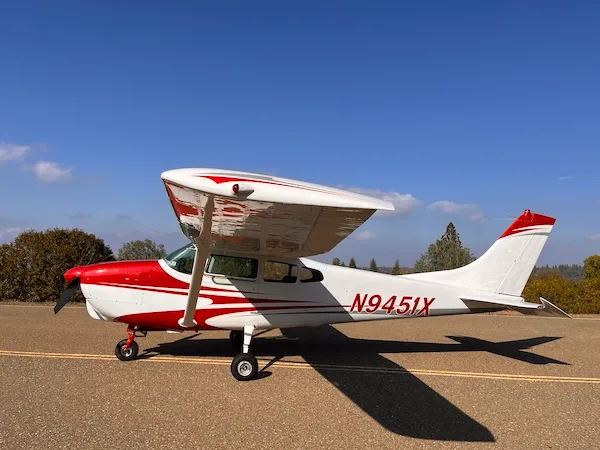 A white and red high-wing single-engine aircraft, N9451X, parked on an asphalt surface under a clear blue sky.