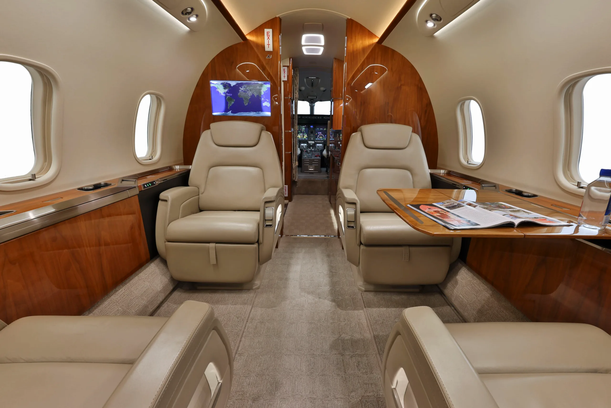 The elegant cabin interior of a business jet with beige leather seating and a view towards the cockpit.