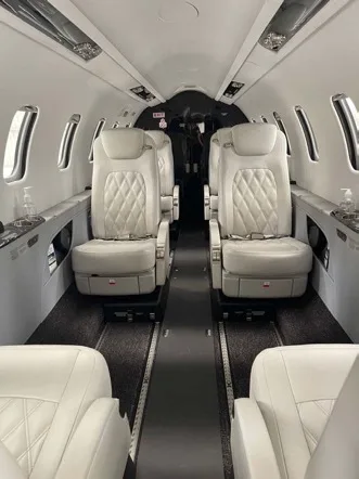 View down the aisle of a private jet cabin with white quilted seats on both sides.