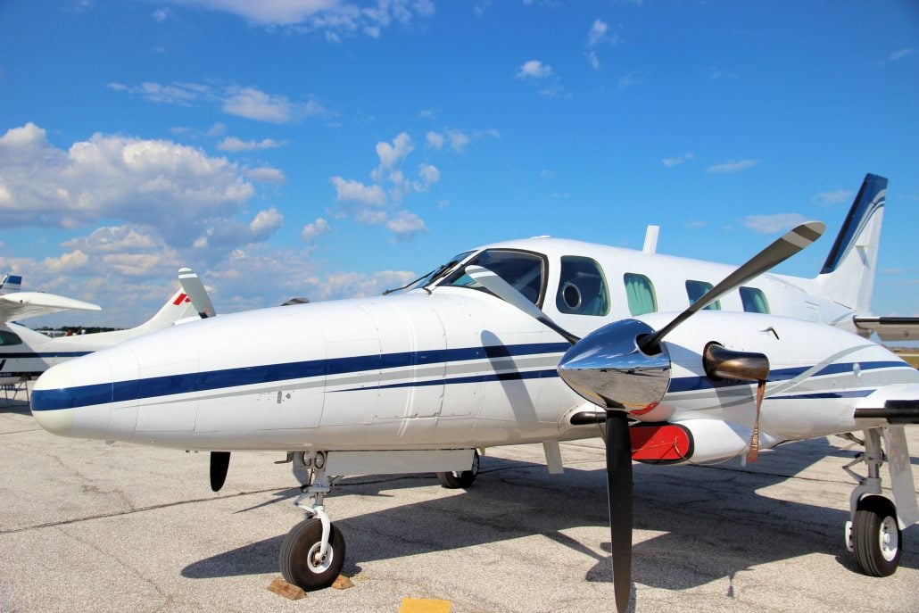 A white and blue single-engine aircraft is parked on the tarmac under a blue sky.