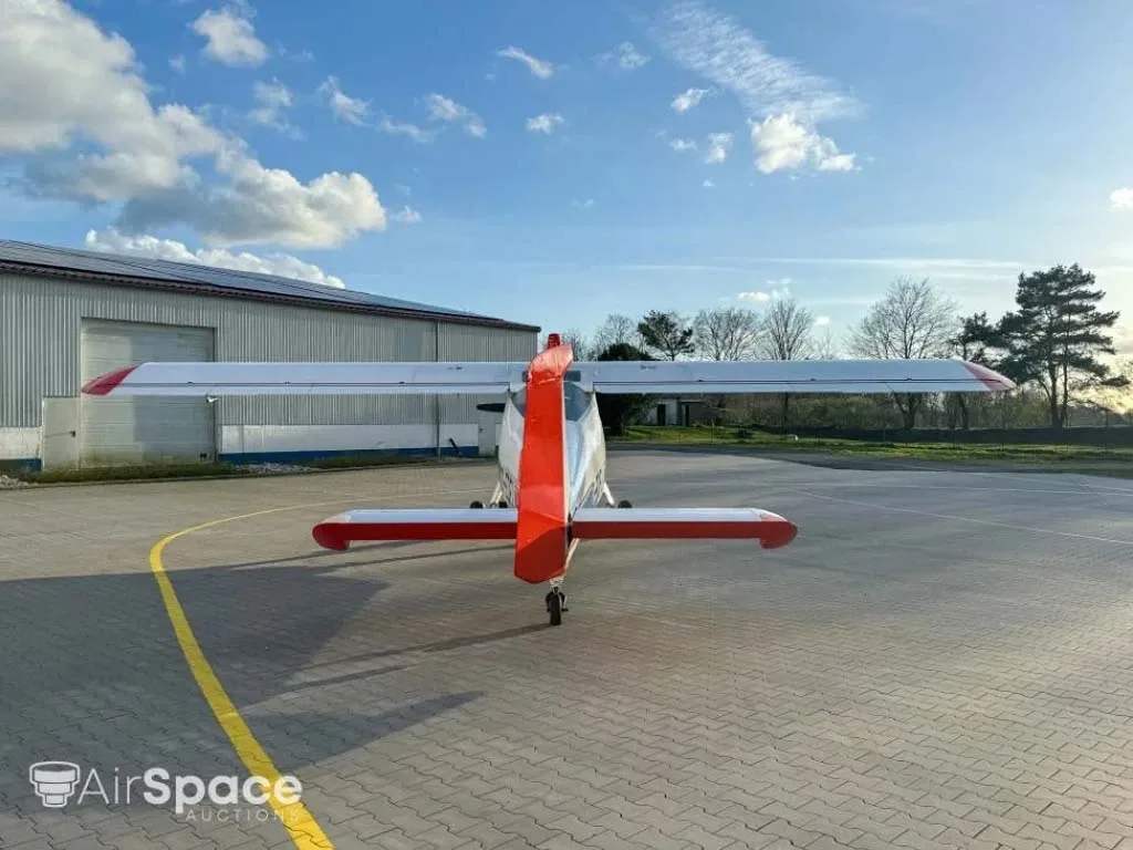 A rear view of a white aircraft with red tail and wingtips, parked on a paved apron with a yellow line.