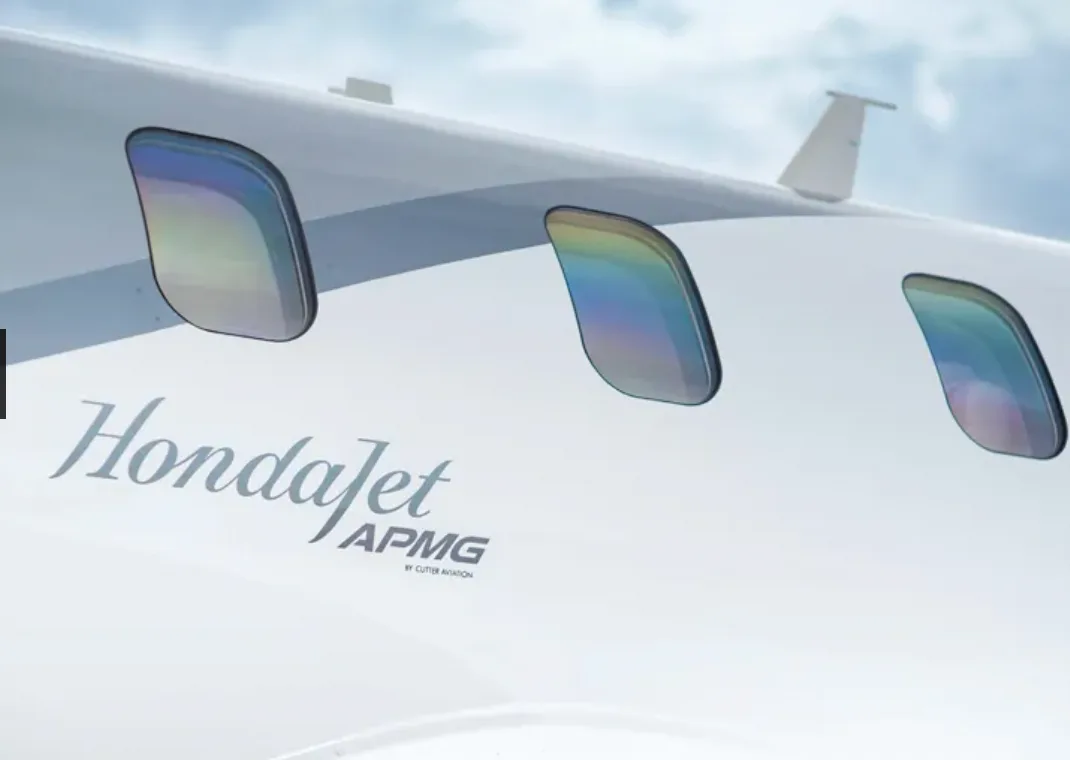 A HondaJet aircraft in a grey and white paint scheme, parked on a tarmac at sunset.