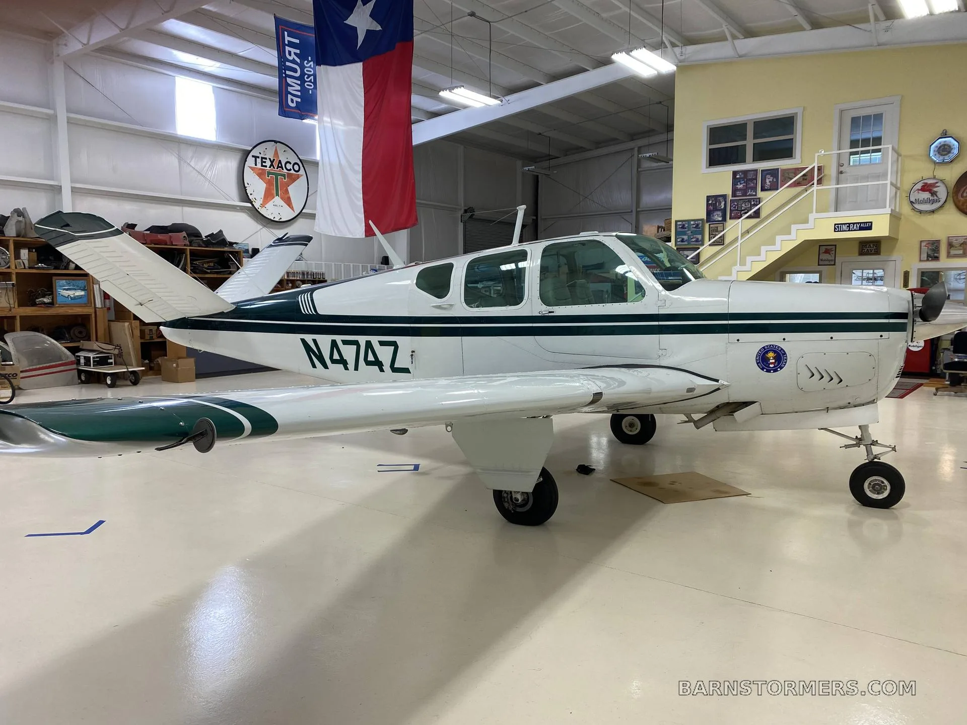 A white and dark green Beechcraft Bonanza with registration N474Z is parked in a hangar, viewed from the side.
