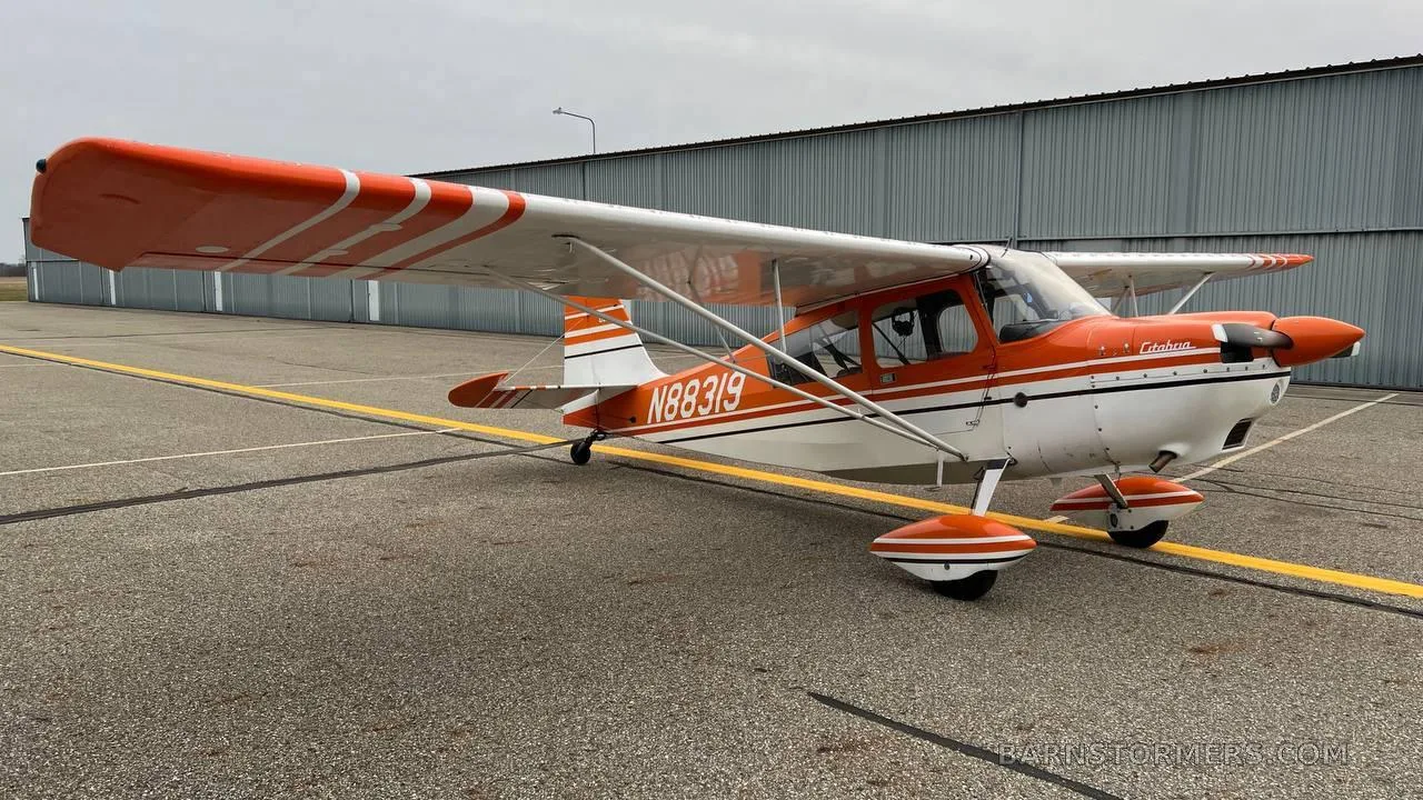 A three-quarter front view of an orange and white Cessna 170B aircraft with tail number N88319 parked on an asphalt apron.