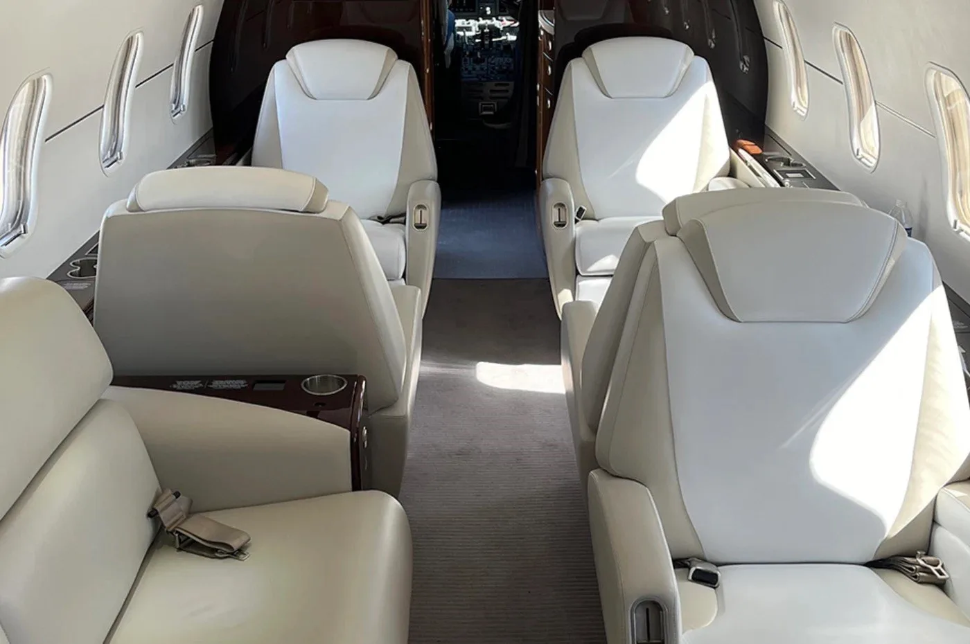 The luxurious interior cabin of a business jet, with light-colored leather seats and a view towards the cockpit.