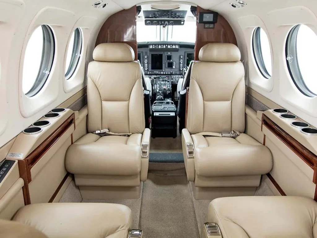 The beige leather interior of an aircraft cabin, looking forward towards the cockpit, with two rows of seats visible.
