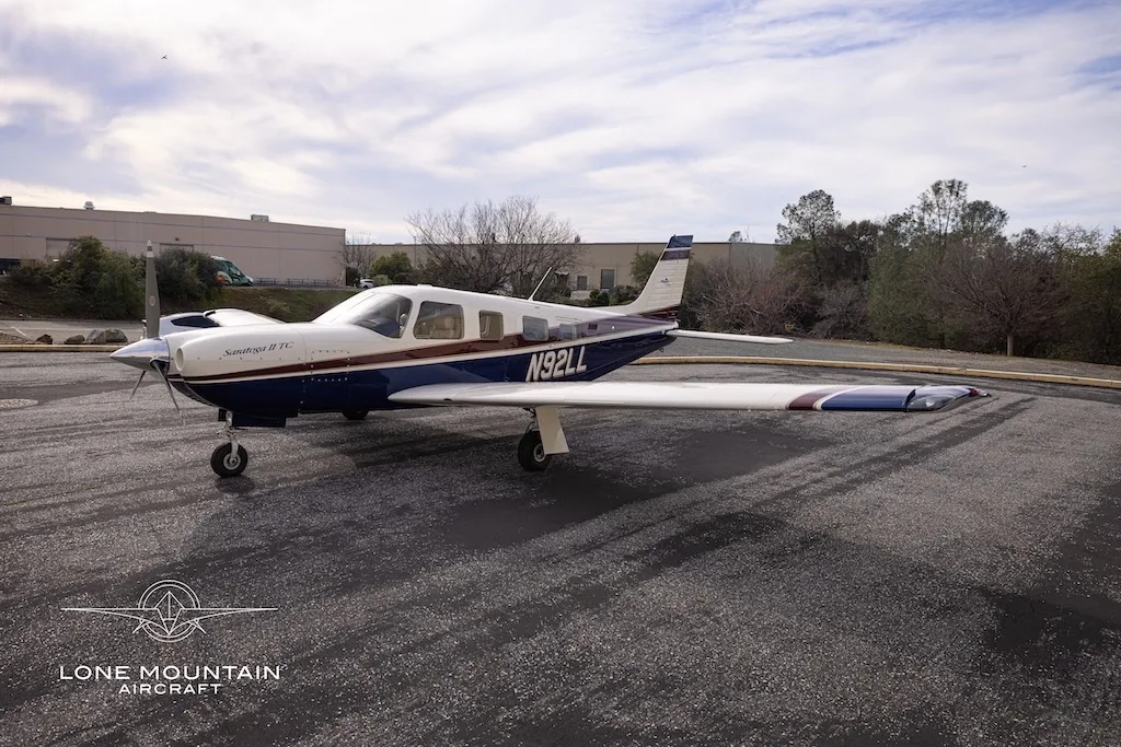 A three-quarter front view of the Piper Saratoga II TC aircraft (N92LL) with blue and white paint scheme parked on an asphalt apron.
