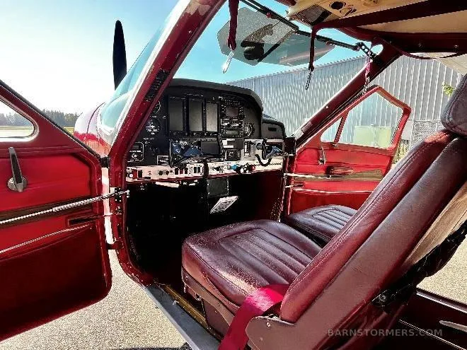 The open cockpit of a red aircraft, showing brown leather seats and the instrument panel.