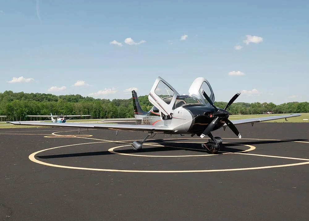 A three-quarter front view of the silver and black Cirrus SR22 aircraft N816RJ with its gull-wing doors open, parked on an airfield.