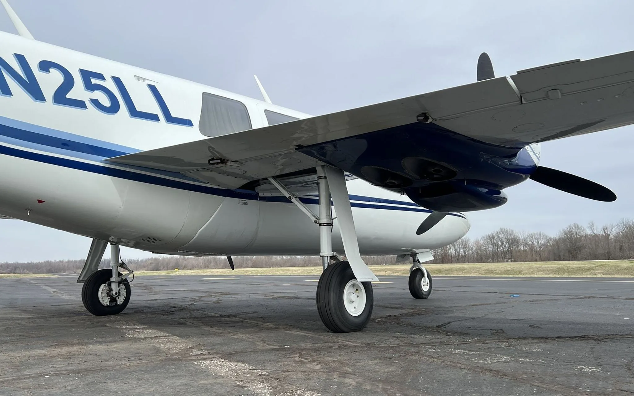 Close-up view of the main landing gear and fuselage of the N25LL aircraft, showing the blue stripe and registration.