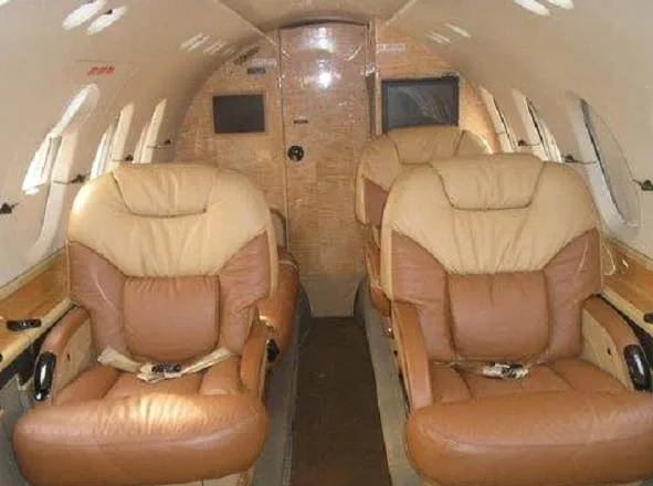 The interior cabin of a private jet with tan and brown leather seats, looking towards the rear.